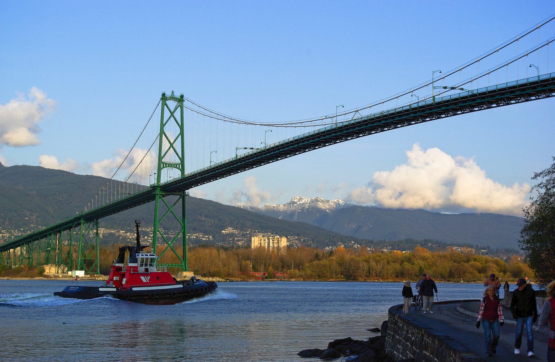 A tugboat passing under the Lions Gate Bridge, with the North Shore mountains behind.