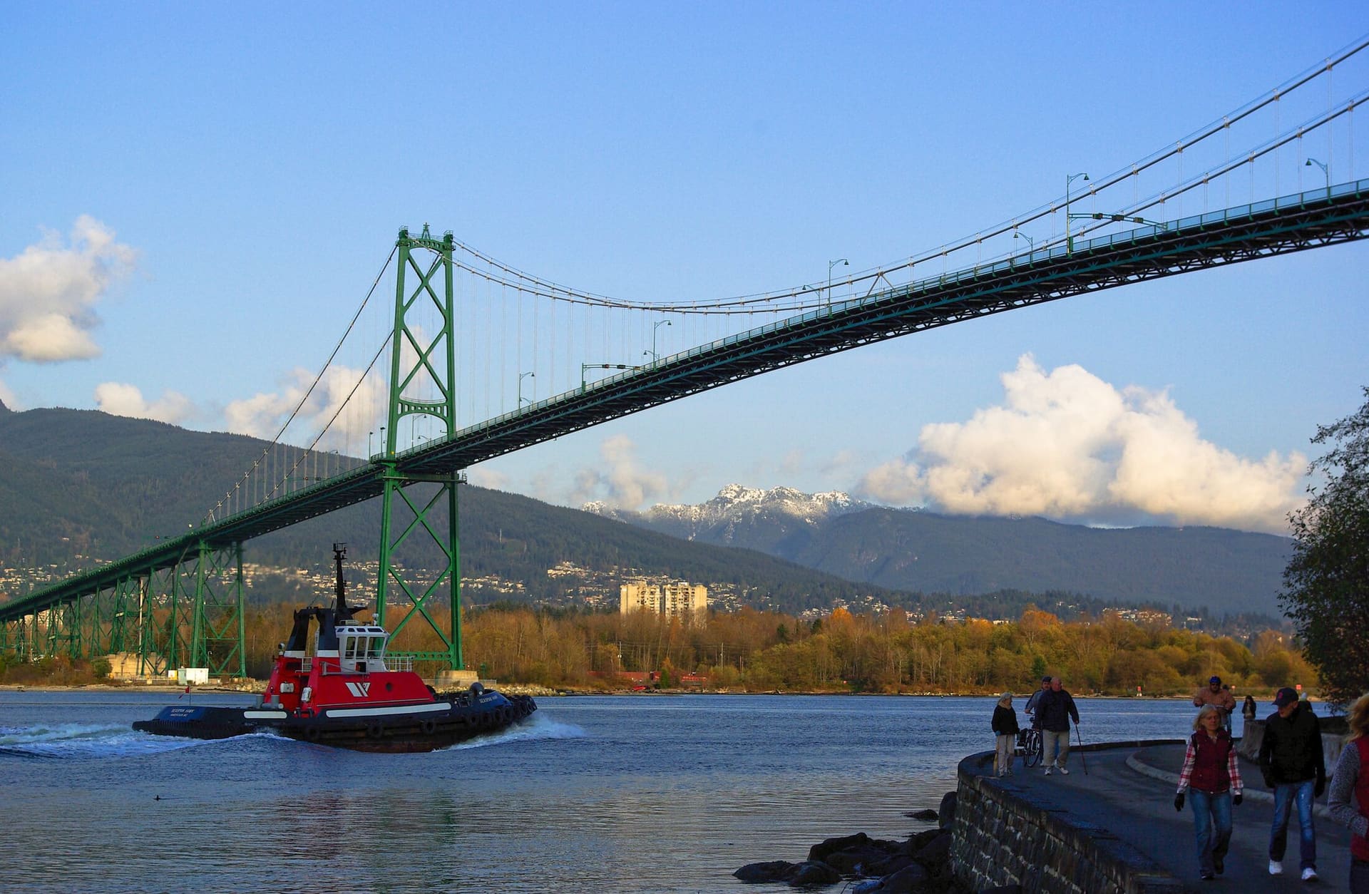 A tugboat passing under the Lions Gate Bridge, with the North Shore mountains behind.