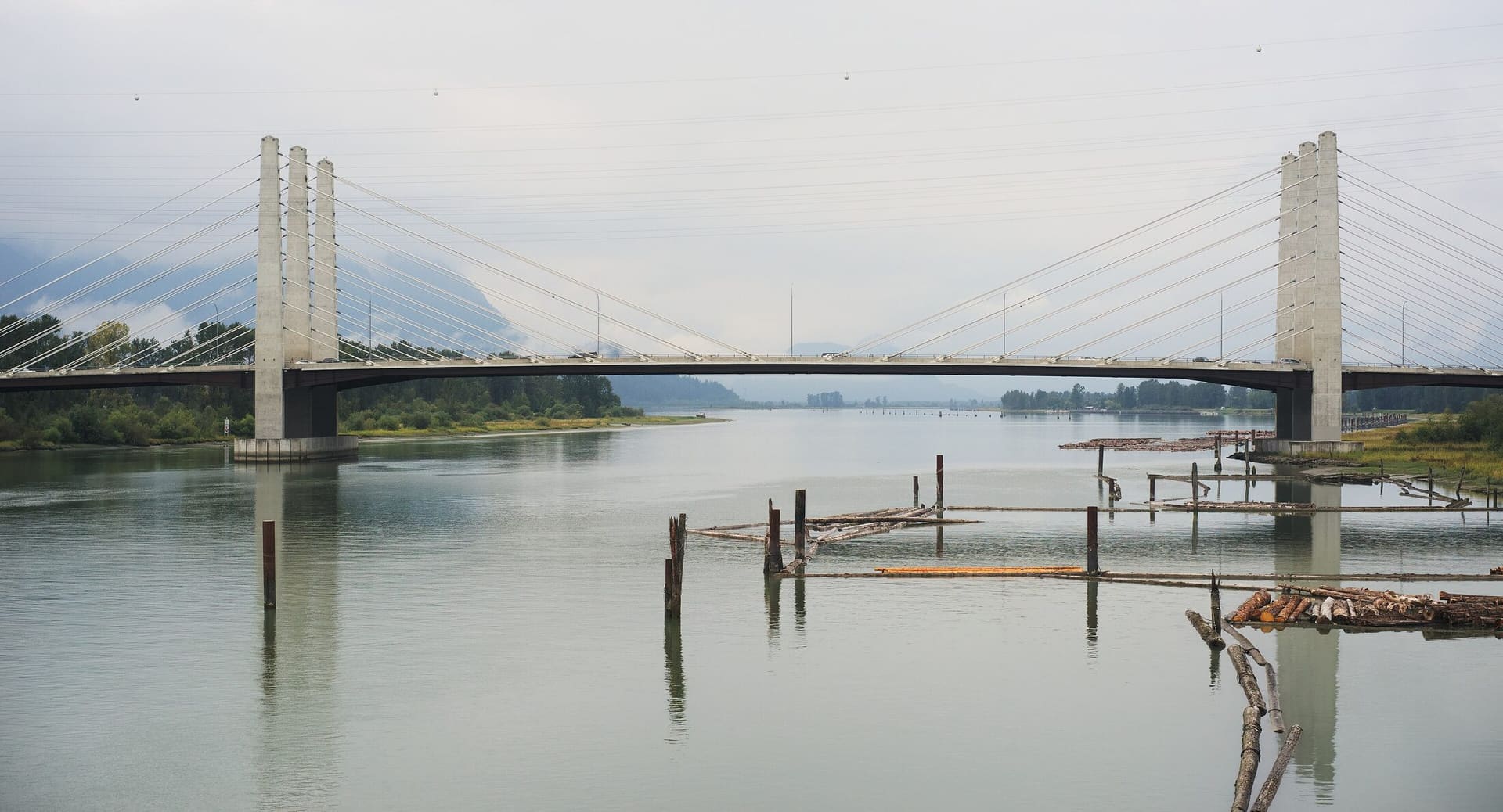 The cable-stayed Pitt River Bridge crossing a calm, grey river, with mountains behind.